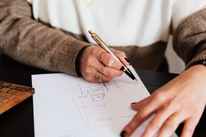 Person in brown sweater writing design sketches on paper next to a wooden keyboard.