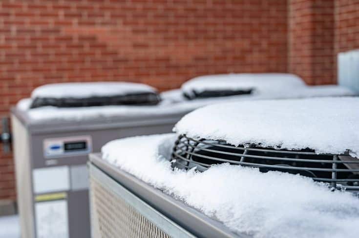 Snow-covered HVAC units outside a brick building, highlighting winter maintenance needs.