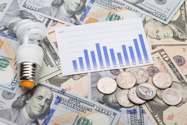 LED bulb, graph, and US currency illustrate energy cost trends and savings.