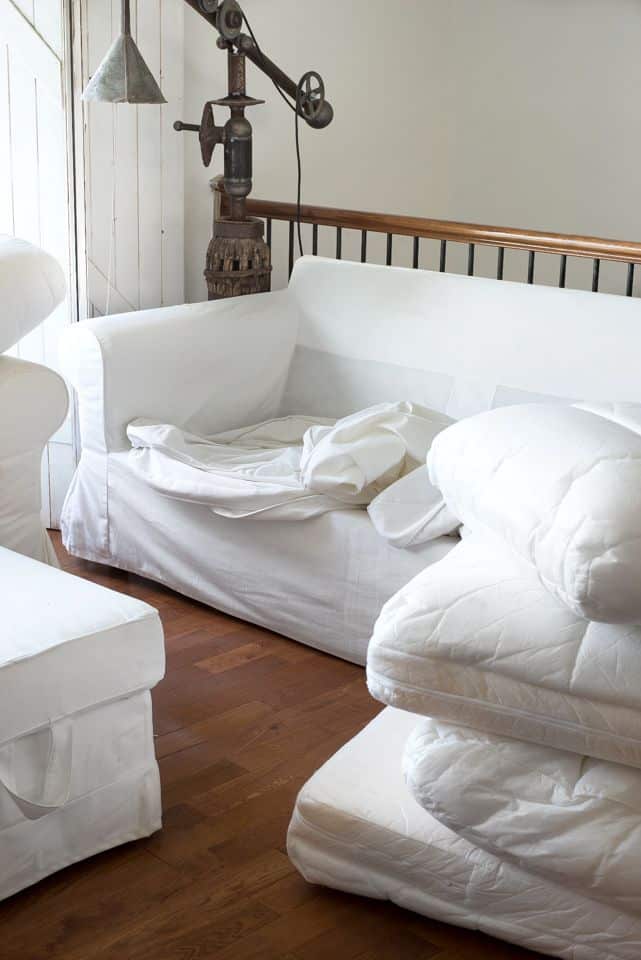 How to clean IKEA couch covers and keep them white - Funky Junk Interiors White couch with disassembled parts and vintage machine decor against wooden floor backdrop. | Sky Rye Design White couch with disassembled parts and vintage machine decor against wooden floor backdrop.