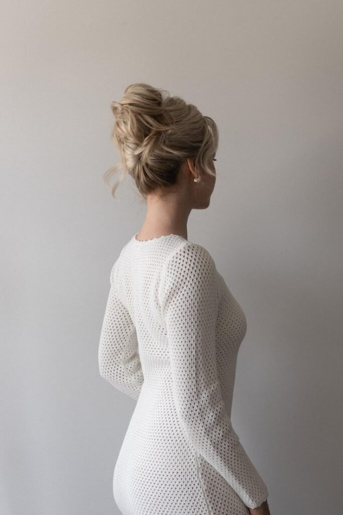Blonde woman in white dress with updo hairstyle, facing away.