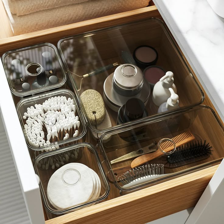 Organized bathroom drawer with toiletries, makeup, cotton swabs, and grooming tools in clear containers.