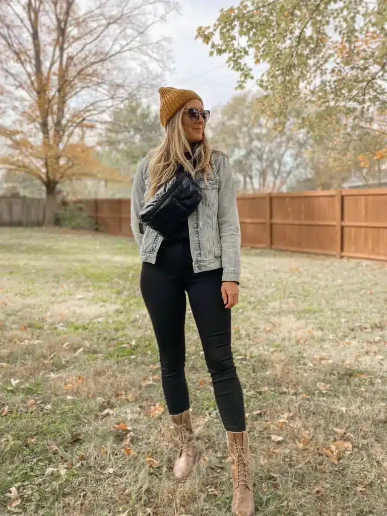 Woman in autumn outfit with denim jacket and beanie stands outdoors in grassy yard.