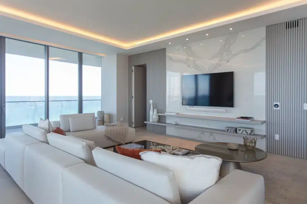 Modern luxury living room with sleek decor, large TV, and ocean views through expansive glass windows.