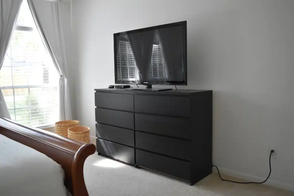 Sleek black dresser with flatscreen TV in a bright, minimalist bedroom setting.