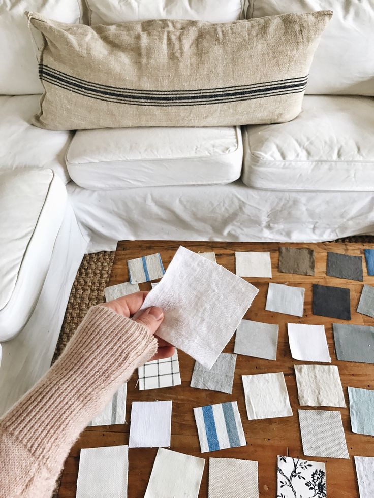 Processed with VSCO with a6 preset Person selecting fabric swatches on a wooden table for home decor inspiration, near a white couch with a striped pillow. | Sky Rye Design Person selecting fabric swatches on a wooden table for home decor inspiration, near a white couch with a striped pillow.
