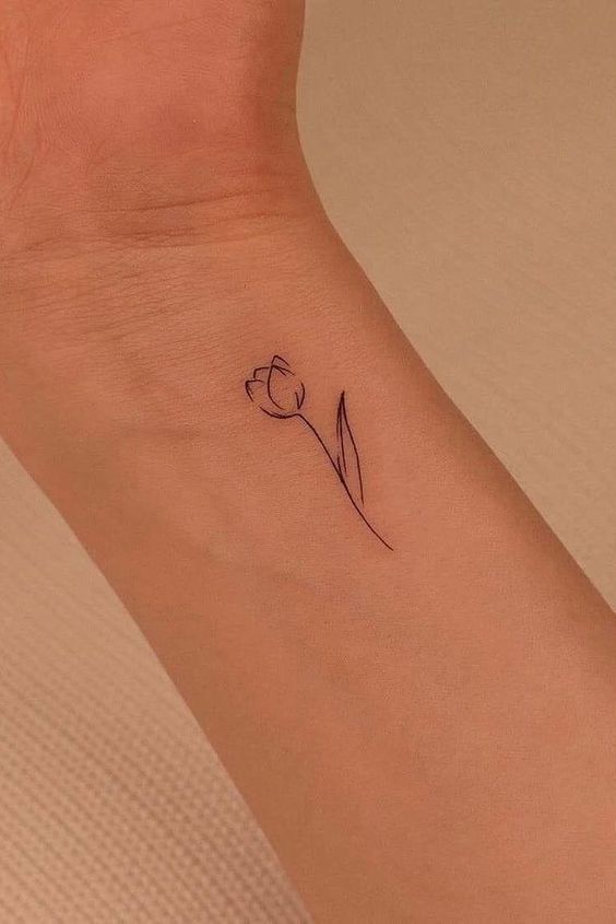 Minimalist tulip tattoo on inner wrist, showcasing delicate line art on skin.