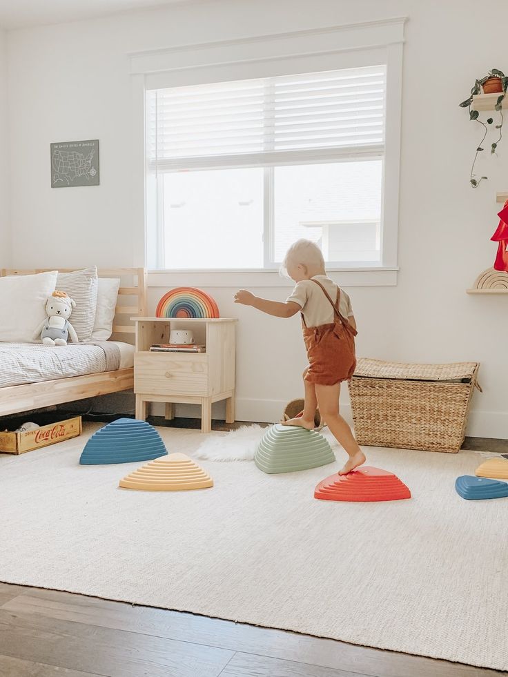 Child playing on colorful stepping stones in a cozy, sunlit bedroom with toys and a bed.
