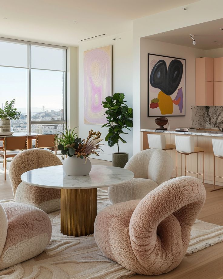 Modern living room with plush chairs, round marble table, abstract art, and large window view.