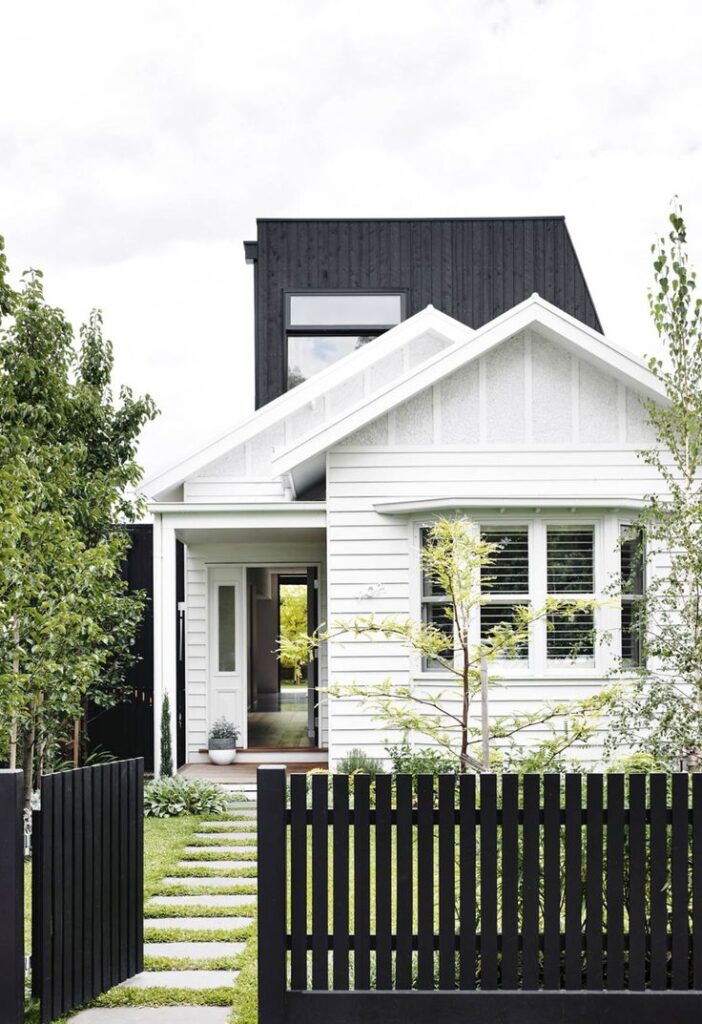 Modern white house with black accents, front garden, and black wooden fence.