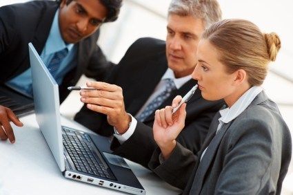 Three business professionals collaborating over a laptop in a meeting.