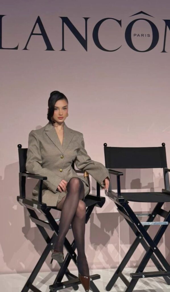 Fashionably dressed woman sitting on a director's chair at a Lancôme event, embodying elegance and style.