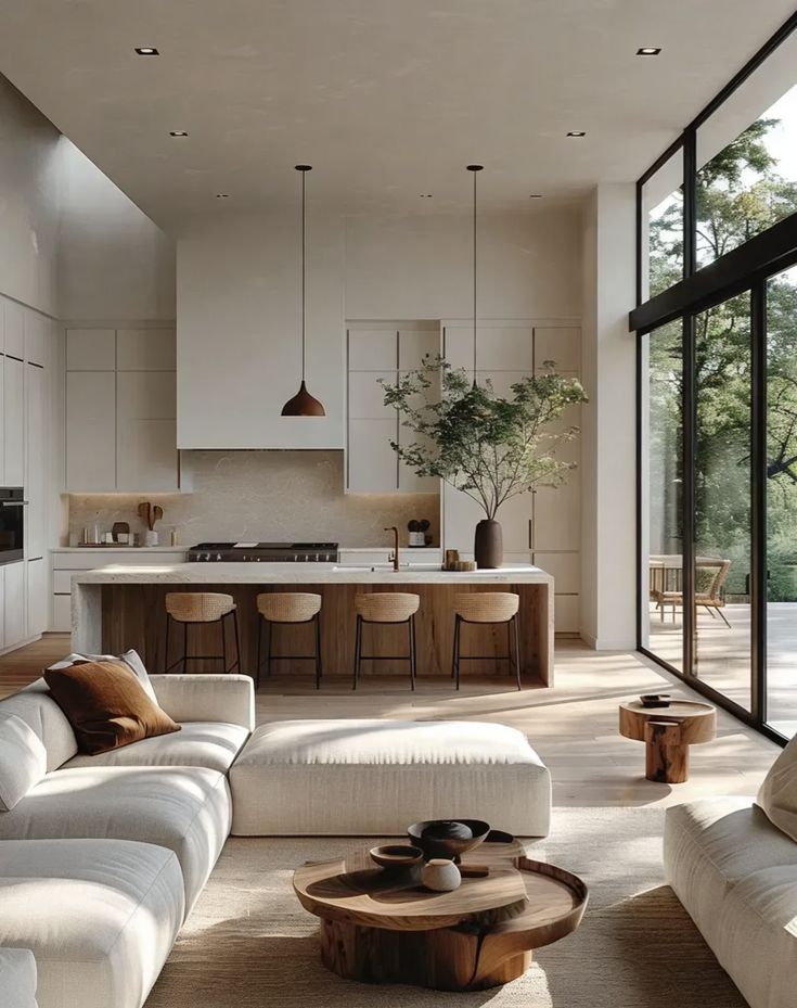 Modern open-concept living room and kitchen with natural light, minimalist decor, and large windows overlooking greenery.
