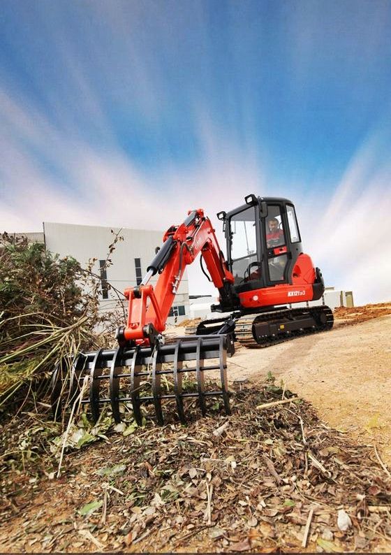 Red excavator clearing brush on a construction site under a bright blue sky.