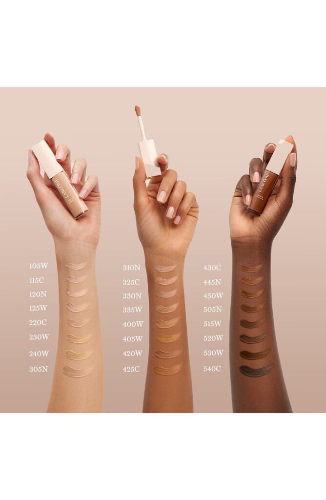 Diverse skin tone concealer swatches displayed on three arms, each holding a concealer tube labeled with shades.