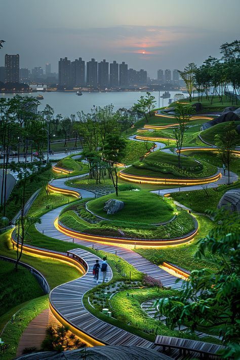 Illuminated serpentine walkway through a green park at dusk with city skyline and river in the background.