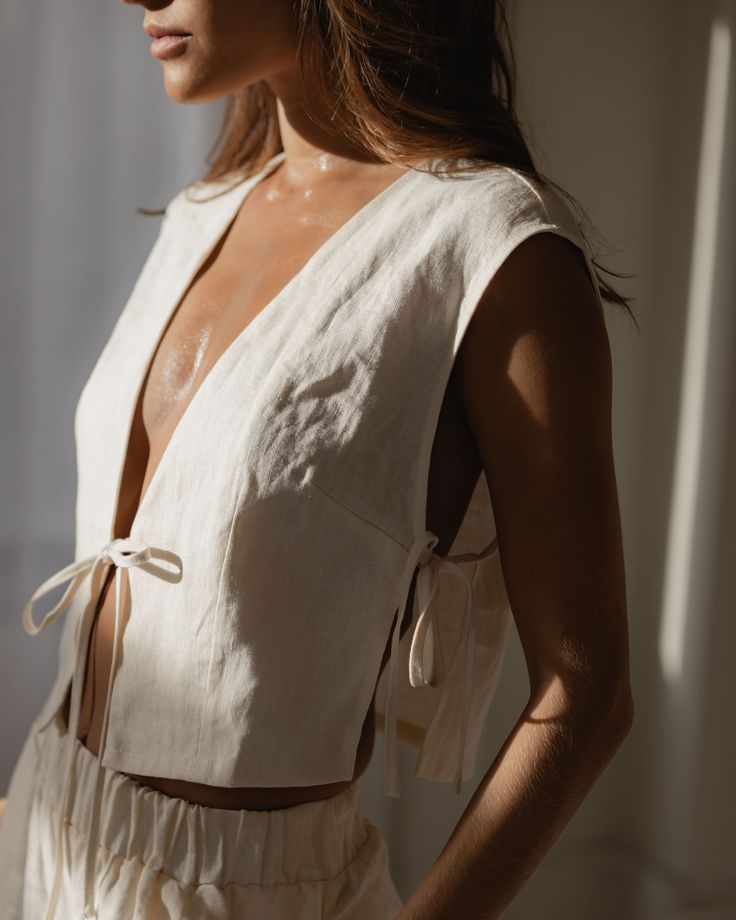 Linen sets are our all-time favourite spring outfit__For the beach the city and lounging at home 🤍__linenset whitelinen linenclothing canadianbrand tietop Side view of a woman in a sleeveless, tied beige vest and shorts in natural lighting. | Sky Rye Design Side view of a woman in a sleeveless, tied beige vest and shorts in natural lighting.