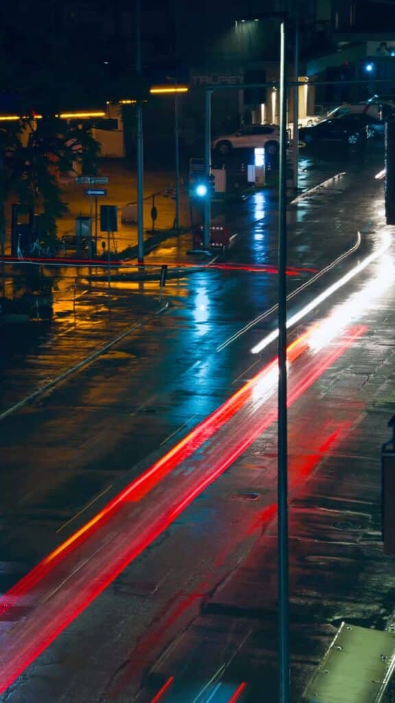 Night street view with blurred car lights on a wet road, creating vibrant red and white light trails.