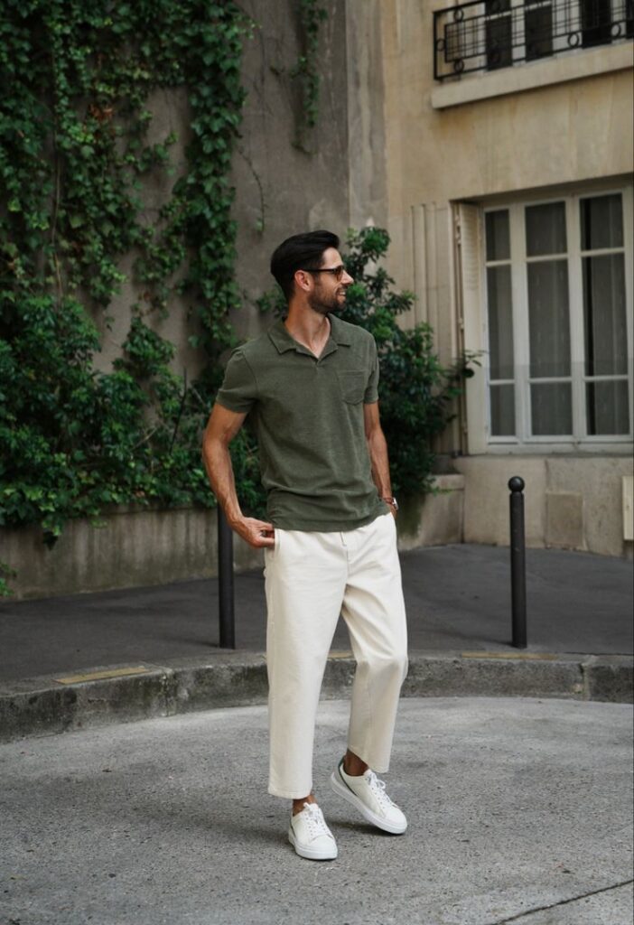 Man in green shirt and white pants walking outdoors, with greenery-covered wall background, stylish casual fashion.