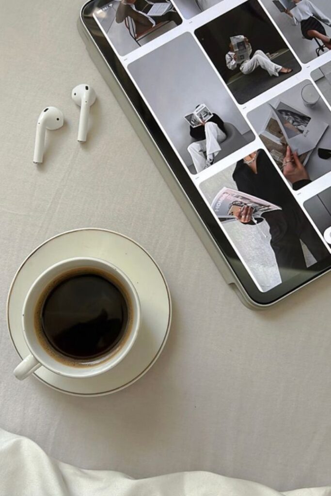 Coffee, earbuds, and a tablet with fashion images on a white surface—perfect morning relaxation setup.