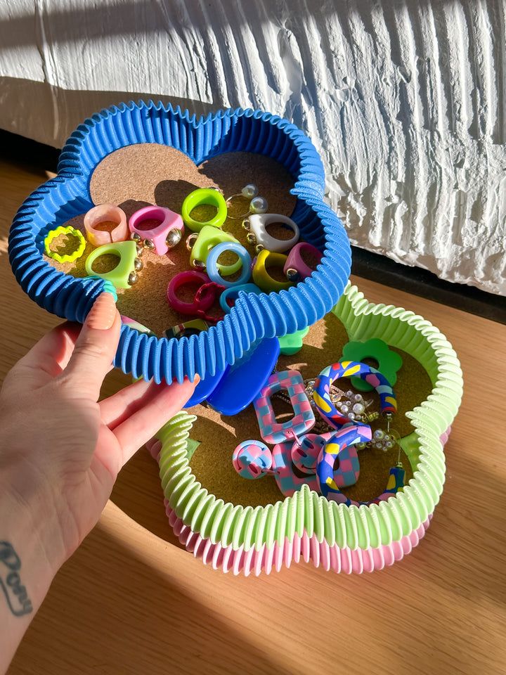 Colorful rings and earrings arranged in flower-shaped, textured trays on a wooden surface.
