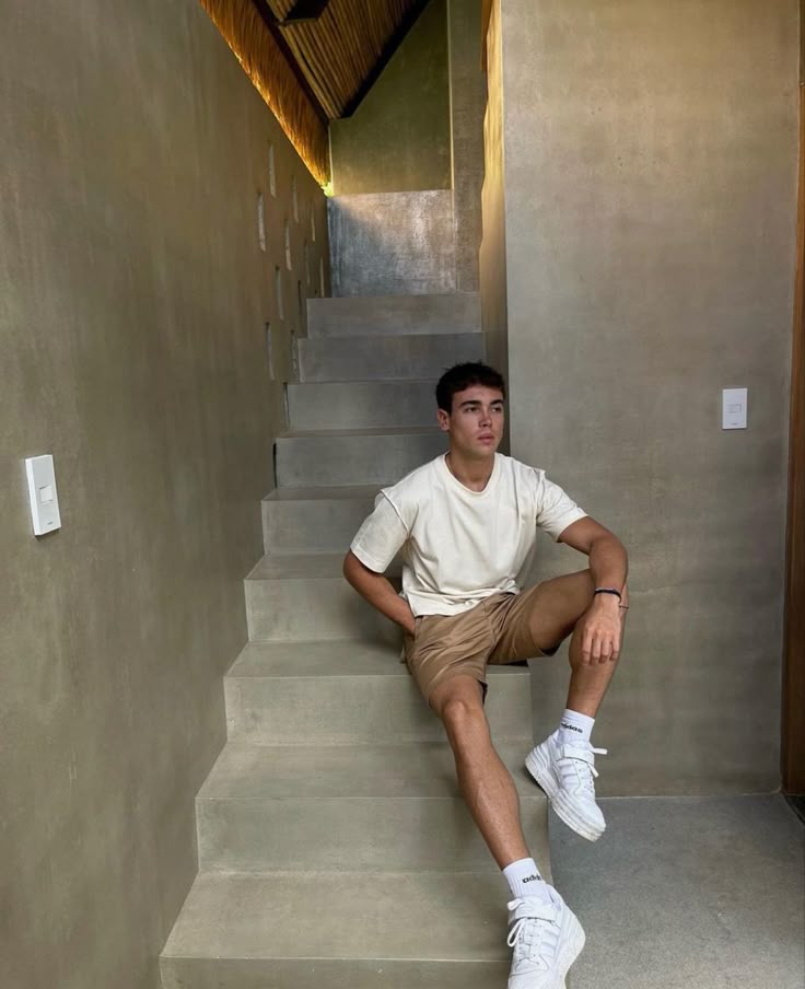 Young man in casual outfit sitting on modern concrete staircase indoors, with natural lighting and minimalist design.