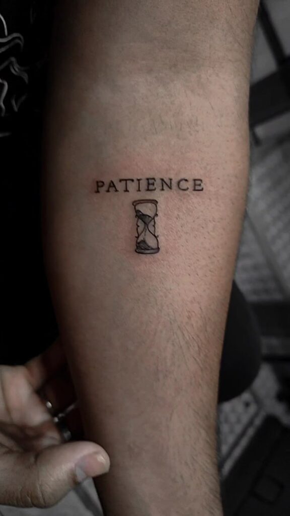 Arm tattoo reading Patience with an hourglass symbol, emphasizing the virtue of patience and time.