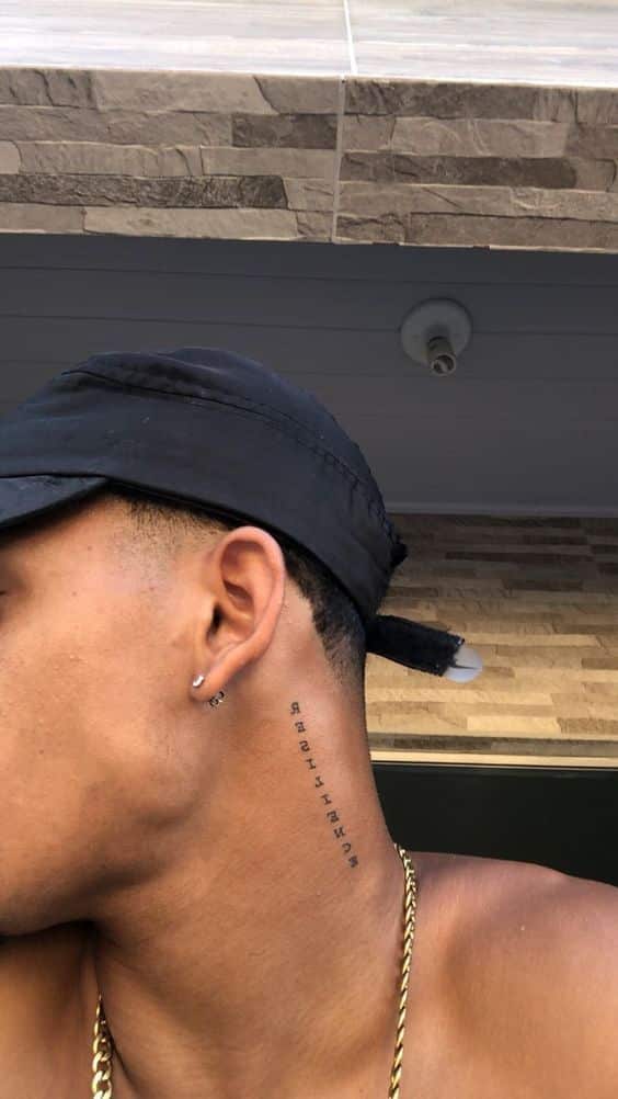 Side view of a person wearing a black cap and chain, showing a vertical neck tattoo with letters.