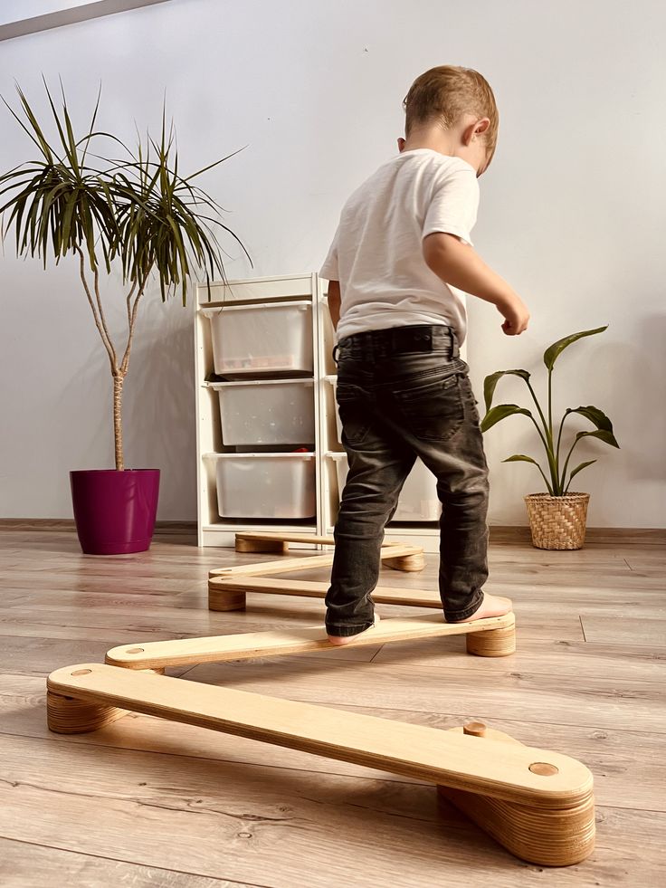 Montessori Balance Set Christmas Gifts for Child Sensory Toys for Toddler Montessori Toys Baby Gifts Child balancing on wooden boards in a modern room with plants and storage shelves. | Sky Rye Design Child balancing on wooden boards in a modern room with plants and storage shelves.