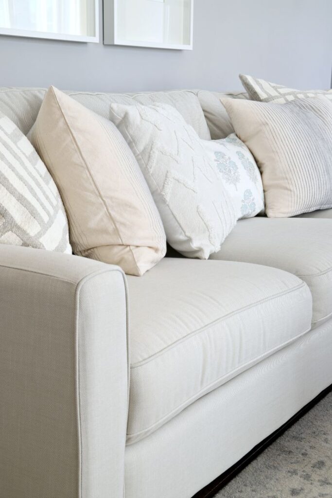 Elegant beige sofa with decorative pillows in neutral tones, creating a cozy and modern living room atmosphere.