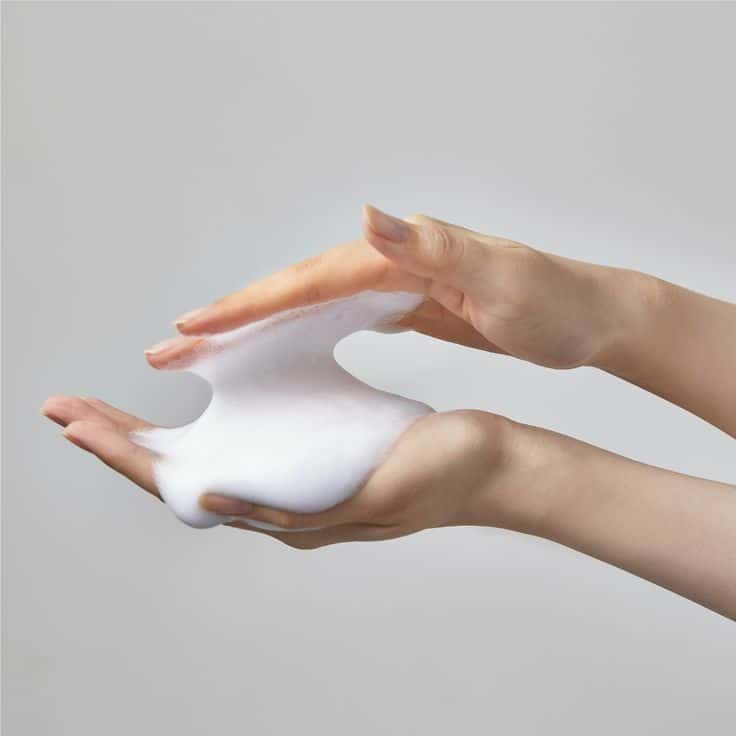 Hands holding and stretching fluffy white foam against a pale background.