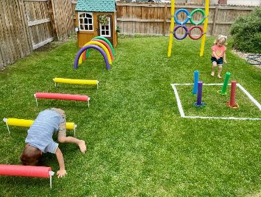 Children playing in backyard obstacle course with colorful hoops and tunnels.