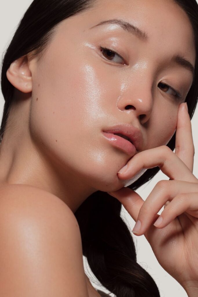 Young woman with glowing skin, touching her face, showcasing a skincare routine.