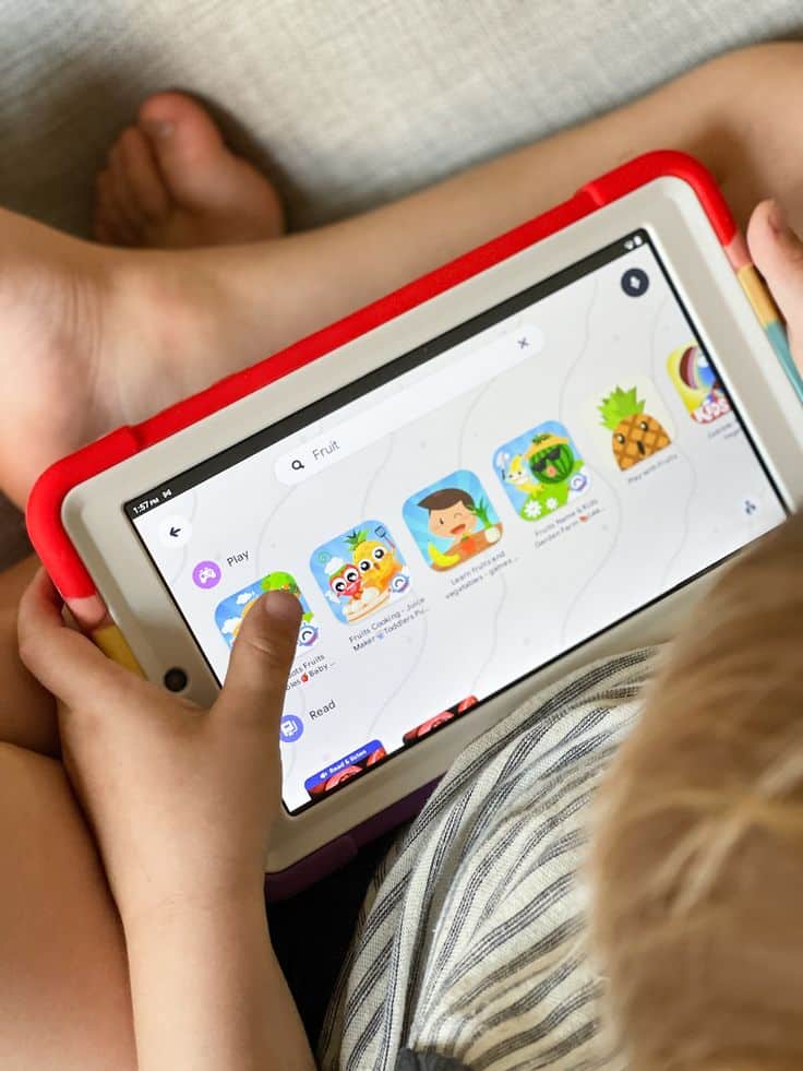Child using a tablet to explore educational apps with a focus on fruit-themed games.