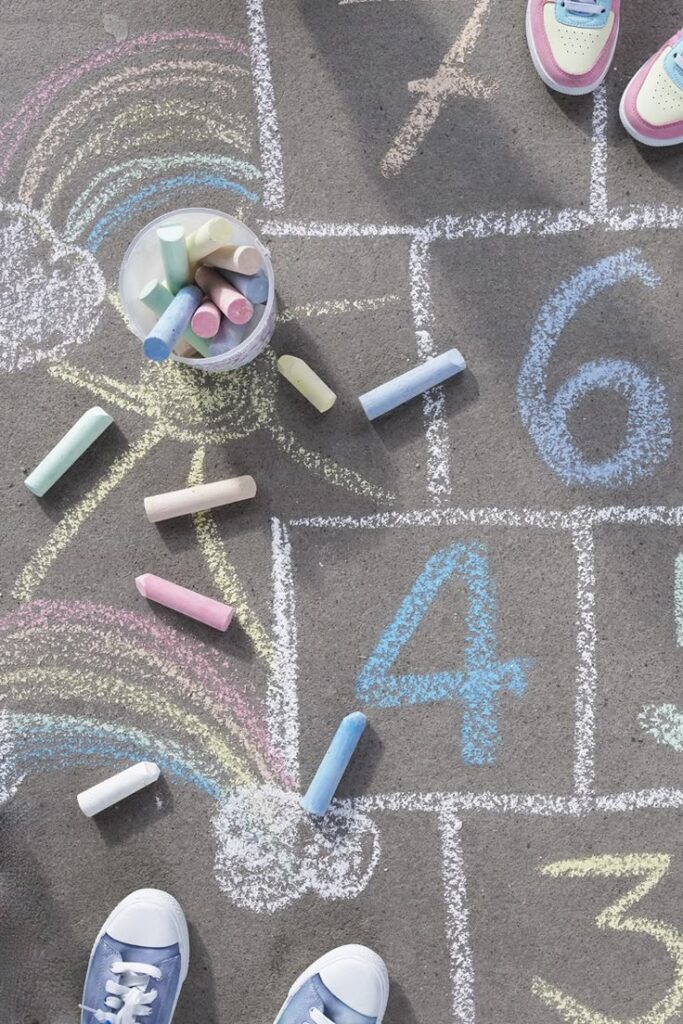 Colorful chalk hopscotch game on pavement with children's shoes and playful rainbow drawing.