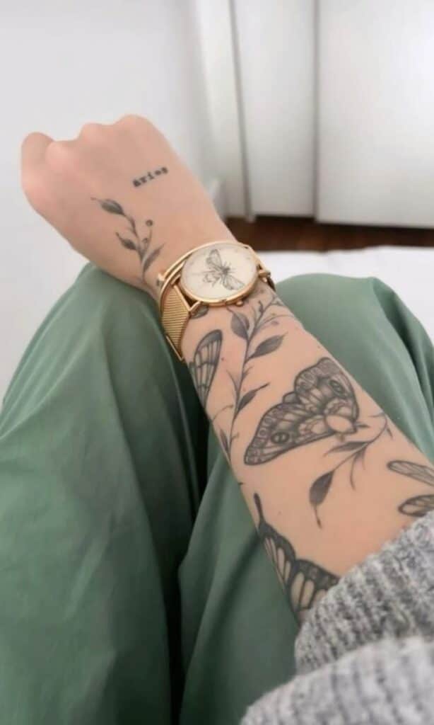 Arm adorned with floral tattoos and a butterfly watch, wrapped in green fabric.