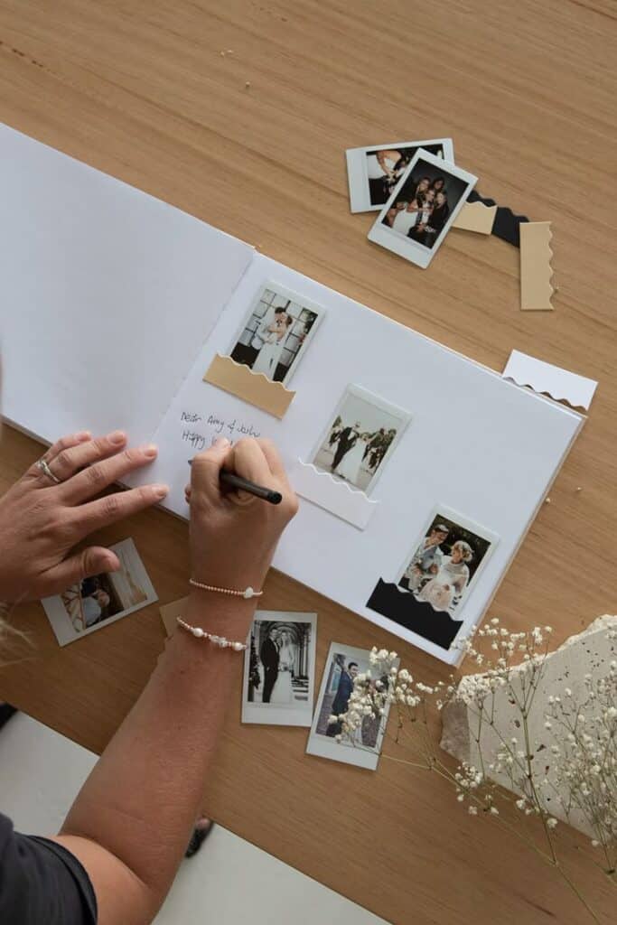 Creating a wedding photo album with instant photos and handwritten notes on a wooden table.