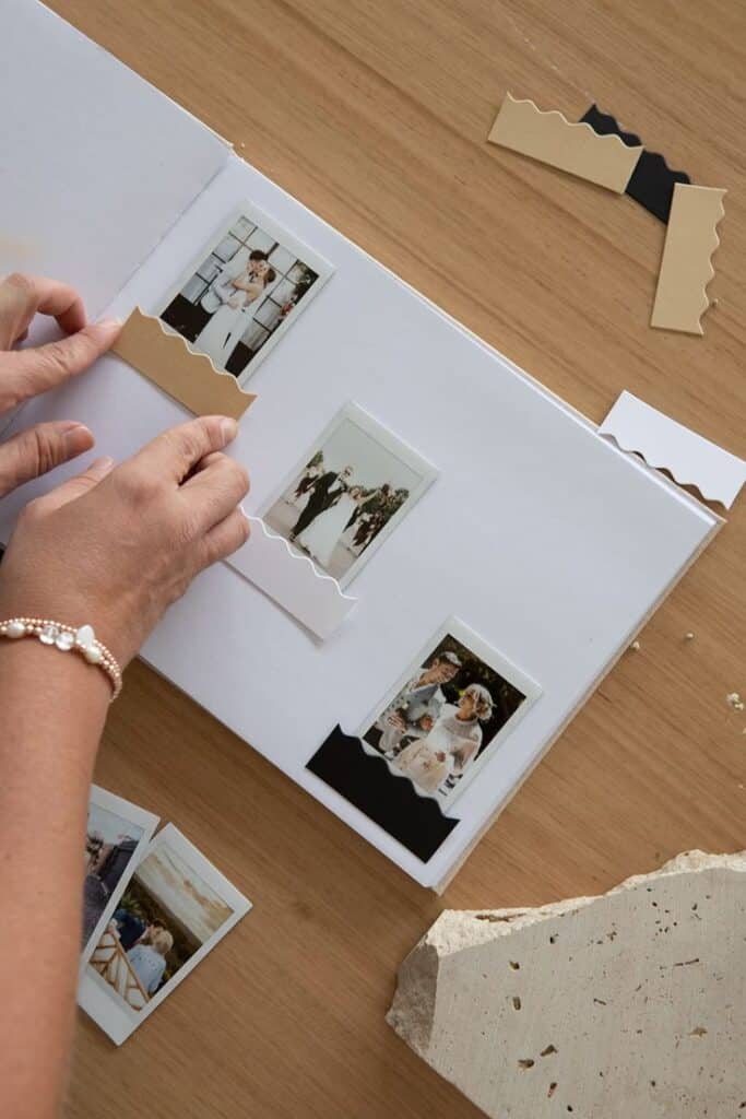 Creating a wedding photo album with instant film prints and decorative borders on a wooden table.