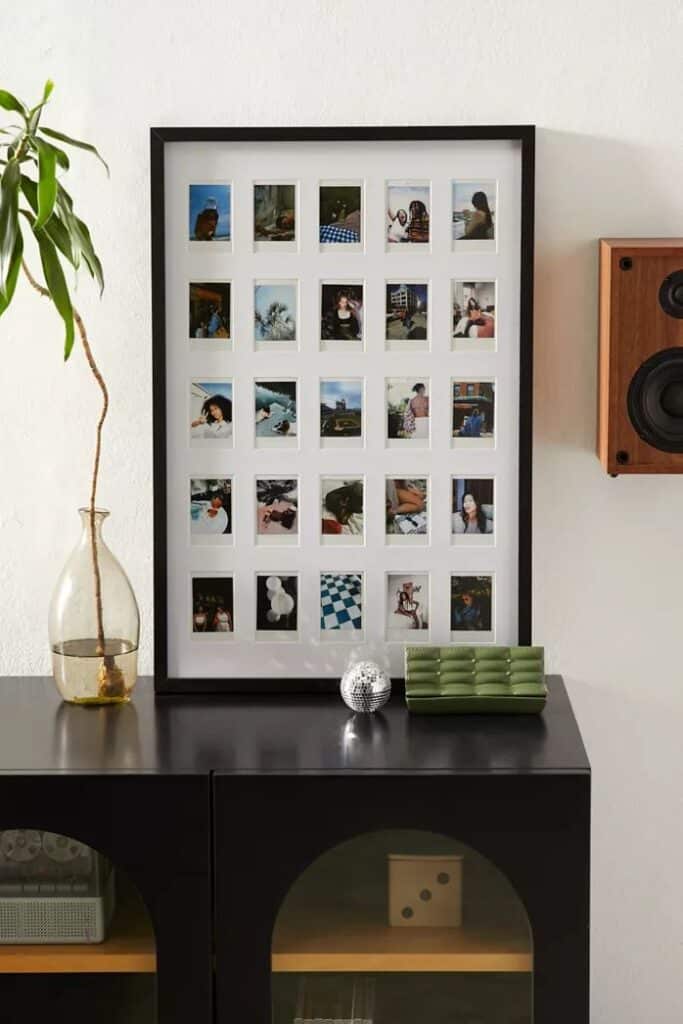 Framed collage of Polaroid photos on a cabinet with decor items, including a plant, vase, and speaker for modern style.