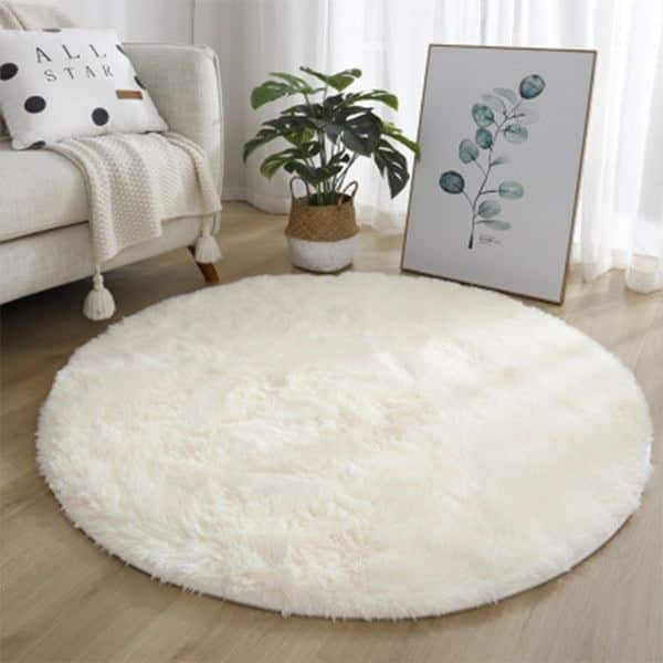 Cozy living room with a round white fluffy rug, leafy plant, framed wall art, and plush sofa.