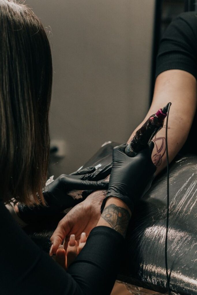 Tattoo artist in gloves creating tattoo on client's arm with a machine, close-up view in a studio setting.