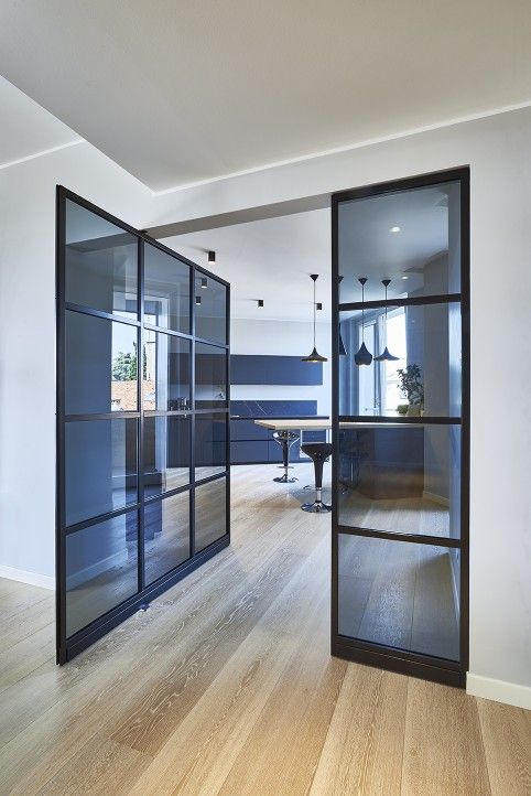 Modern dining room with glass doors, wooden flooring, and pendant lights, showcasing sleek interior decor and ample natural light.