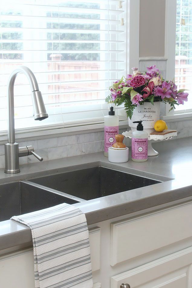 Modern kitchen sink with steel faucet, striped towel, cleaning products, and fresh flowers by the window.