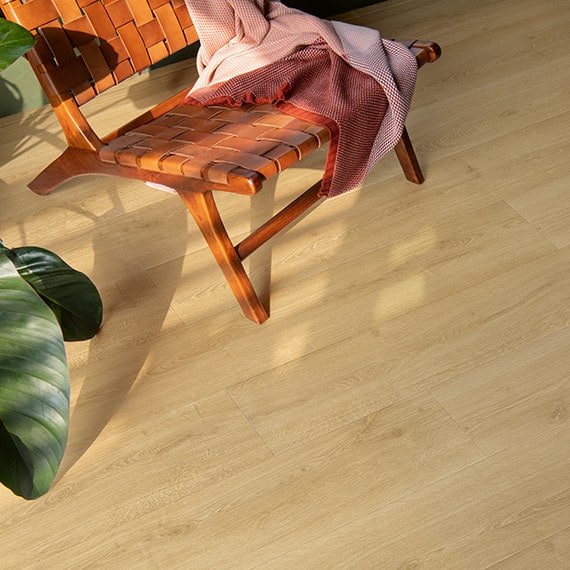 Wooden chair with woven leather seat on light wood flooring, draped with a pink blanket, next to a green plant.
