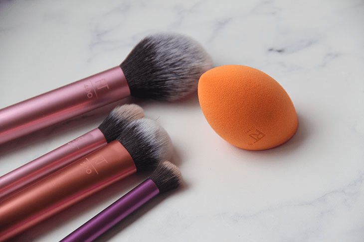Makeup brushes and a sponge blender on a marble surface; essential beauty tools for flawless application.