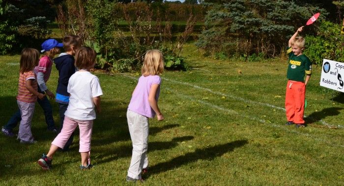 Children playing a game outdoors in a park, with one child holding a paddle, smiling and enjoying the sunny day.
