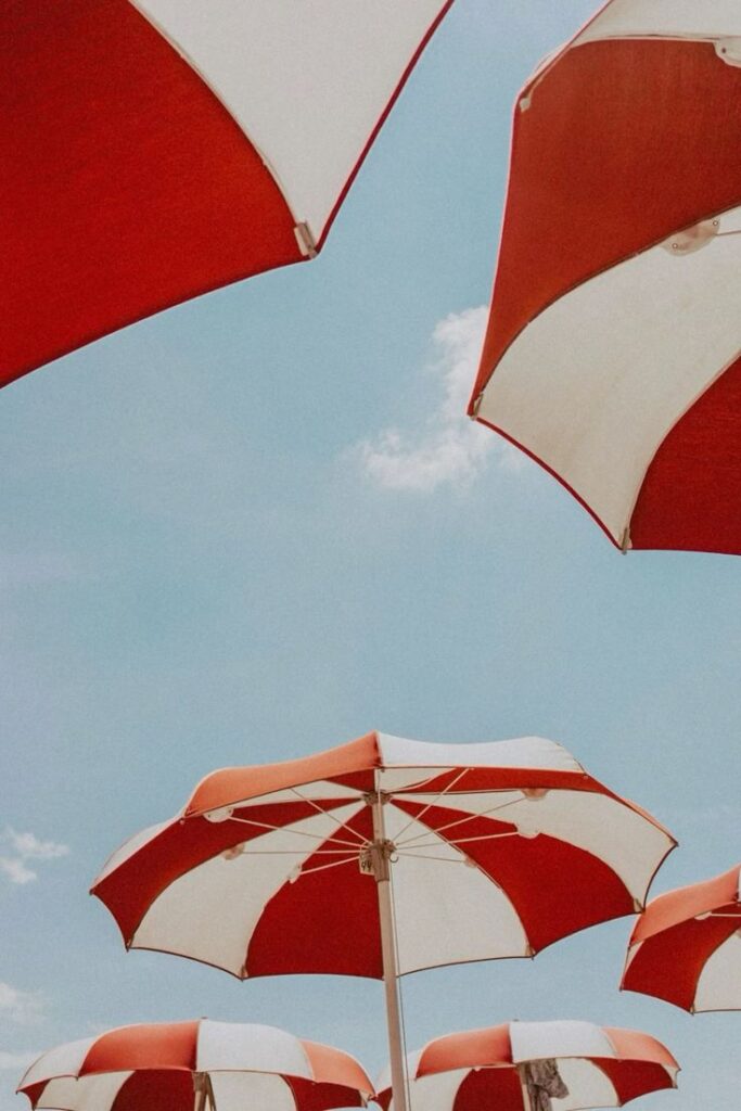 Red and white beach umbrellas against a clear blue sky, capturing a sunny summer day mood.