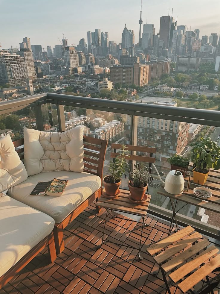 Cozy balcony with plants and seating, overlooking a city skyline under a clear sky, during sunset.