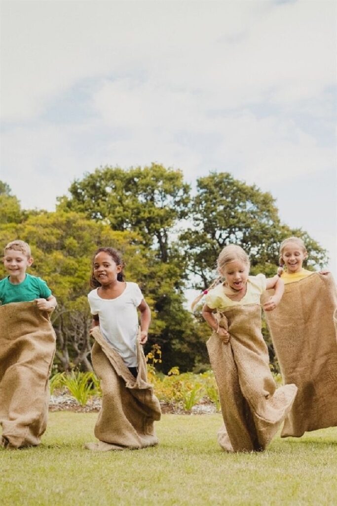 Children enjoying a sack race outdoors on a sunny day in a park.