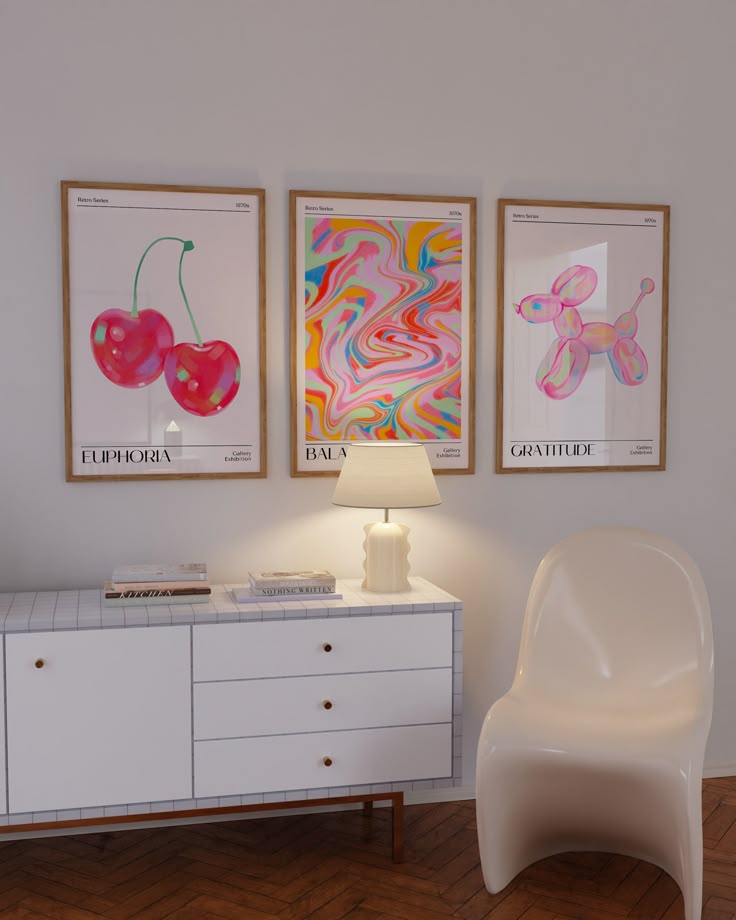 Modern art prints above a white sideboard with a lamp, chair, and books in a stylish, minimalistic room.